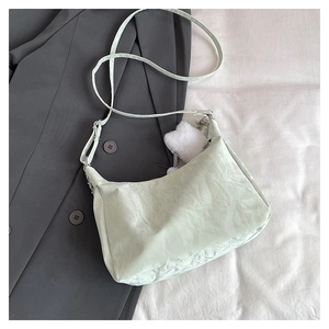 Detail of mint green crescent bag featuring pleated texture and white plush ball charm