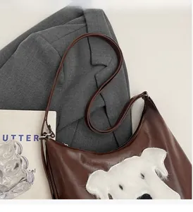 Détail du sac demi-lune marron avec patch chiot en peluche posé sur un blazer gris
