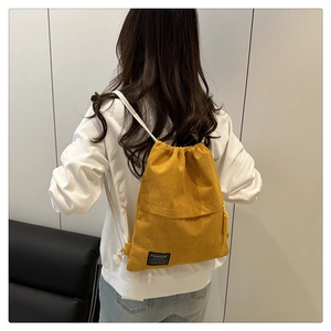Detail of yellow corduroy drawstring backpack showing white cotton rope and fashion patch
