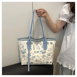 Detail of hand holding beige tote bag with blue trim and cute cartoon graffiti prints