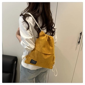 Detailed back view of a yellow corduroy drawstring backpack with cream braided straps