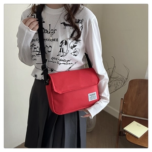 Detail of red oxford canvas messenger bag showing the fashion label and black strap