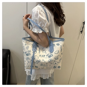 Close-up of a cream tote bag featuring blue graffiti prints and contrasting blue straps
