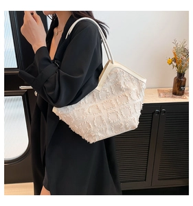 Détail d'un sac cabas blanc cassé à franges carrées porté sur un manteau noir
