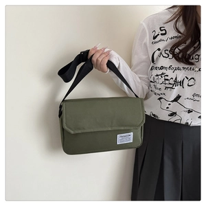 Detail of army green canvas messenger bag featuring a white brand label and black strap