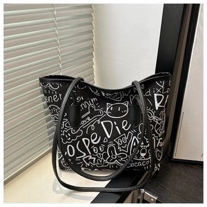 Detailed view of black canvas tote bag with white graffiti prints and leather straps