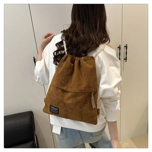 Rear view of a model wearing a brown corduroy drawstring backpack with ribbed texture
