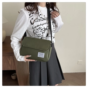 Detail view of a dark green canvas messenger bag worn by a model with wide black strap