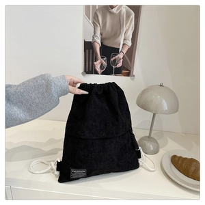 Close-up of black corduroy drawstring backpack on a desk with a fashion label