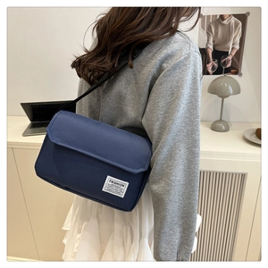 Detail of navy blue oxford fabric shoulder bag with adjustable strap worn by a model