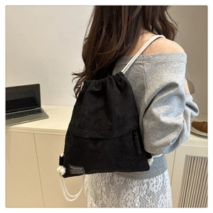 Detail of black corduroy drawstring backpack featuring fashion label and white rope straps