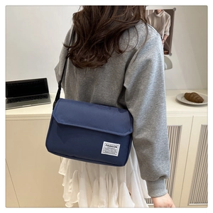 Detail of navy blue crossbody bag with fashion instinct patch worn by a model
