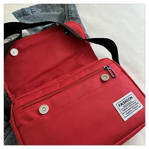 Detail view of red oxford messenger bag with silver magnetic snap and zipper pocket