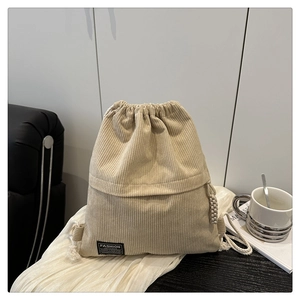 Detail of beige corduroy drawstring backpack with black fashion brand tag on fabric