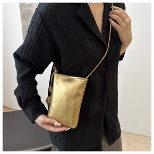Détail d'un sac à bandoulière doré métallisé avec plis texturés et bandoulière chaîne