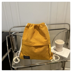 Close-up of yellow corduroy drawstring backpack on a metal stand with fashion label detail