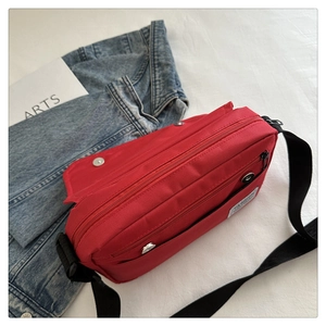 Detail view of red oxford fabric crossbody bag featuring multiple zipper pockets and flap