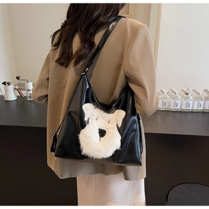 Détail d'un sac à bandoulière noir brillant avec un écusson en peluche de chien schnauzer