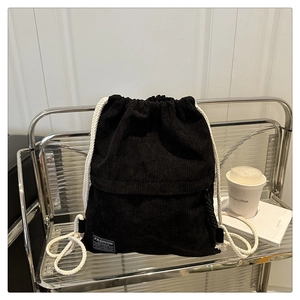 Detail of black corduroy drawstring backpack with white rope straps and fashion patch