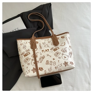 Detail of a large cream tote bag with brown graffiti patterns and leather shoulder straps