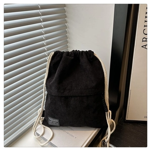 Detail of black corduroy drawstring backpack showing texture and fashion brand label