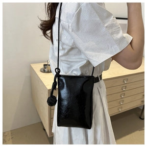 Détail du sac de téléphone noir brillant avec nœud à boule tressée sur la sangle
