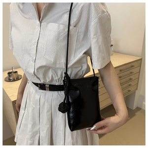 Détail d'un mini sac noir brillant avec bandoulière et décoration de nœud tissé