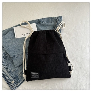 Detail of black corduroy drawstring backpack with cotton ropes on denim jacket