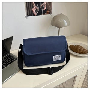 Detail view of a navy blue canvas messenger bag with a wide nylon strap on a white desk