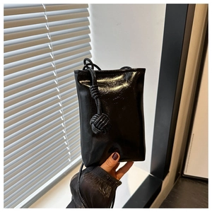 Détail d'un mini sac de téléphone noir en cuir verni brillant avec un nœud décoratif