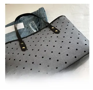 Detailed view of grey polka dot tote bag with black leather handles and gold metal rivets