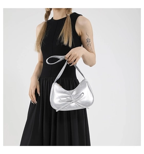 Dettaglio borsa a sella argento metallizzato con fiocco, indossata a spalla dalla modella