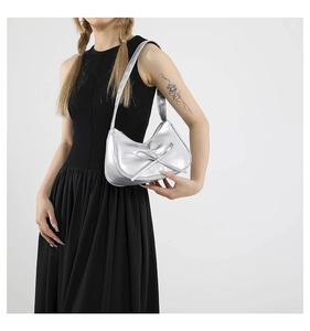 Dettaglio della borsa a spalla argento con fiocco indossata da modella in nero