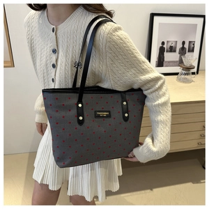 Detail of grey canvas tote bag with red polka dots and black leather straps worn by model