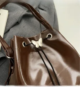 Détail du sac seau en cuir marron foncé avec boucle papillon argentée sur cordon