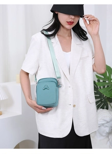 Detail of mint green crossbody phone bag with multi-layer zippers and sporty metal logo