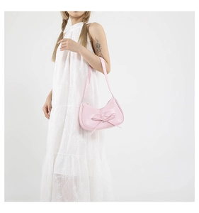 Borsa a spalla rosa con fiocco in pelle indossata da una modella in un abito bianco