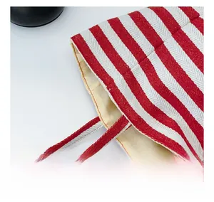 Close-up of precise stitching and red striped fabric handle on this canvas tote bag