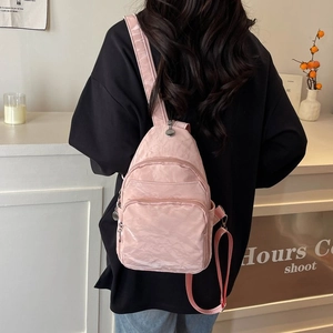 Close-up of light pink nylon crossbody bag with three zipper layers and wide strap