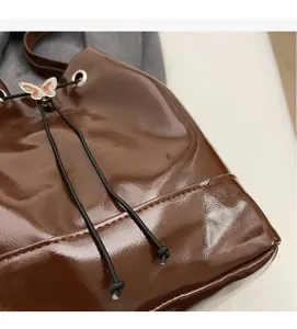 Détail du sac seau marron brillant avec pendentif papillon argenté et cordon de serrage