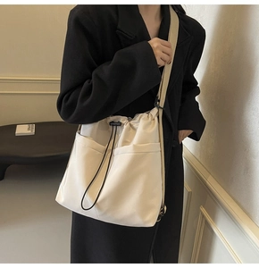 Detail of beige bucket bag showing large capacity and black drawstring closure on shoulder