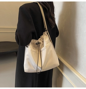 Detail of a large cream crossbody bucket bag with drawstring closure and external pockets