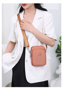Detail of coral pink crossbody phone bag with double zippers and adjustable strap worn by model