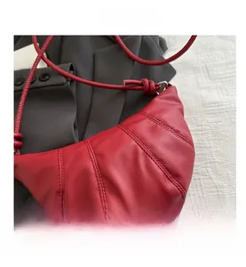 Gros plan du sac croissant en cuir rouge montrant les coutures et la bandoulière