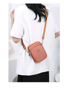 Detail of a matte orange crossbody bag with triple zippers and adjustable sport strap
