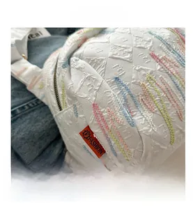 Détail du sac à bandoulière blanc matelassé avec broderies ondulées colorées et étiquette