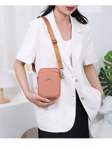 Close-up of peach pink mini crossbody phone bag with metal logo and adjustable strap