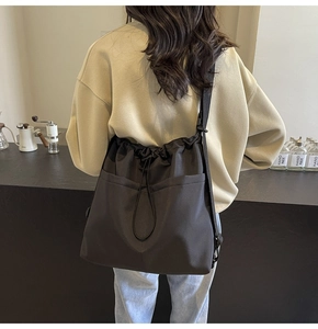 Detail of a large black drawstring bucket bag worn by a model in a cafe setting