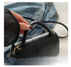 Close-up of black cylinder bag with matte leather, gold D-rings, and padded top handle