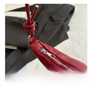 Détail de la fermeture éclair argentée et de la bandoulière nouée du sac en cuir rouge